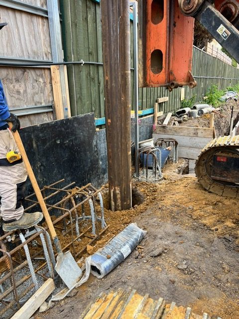 Piling rig drilling deep bored pier in confined residential construction site with reinforcement cages