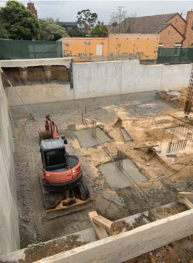 Red excavator in concrete basement pit with reinforcing steel bars and retaining walls
