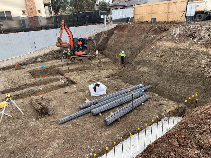 Basement construction site with concrete foundation elements, reinforcement placement, and workers in high-visibility