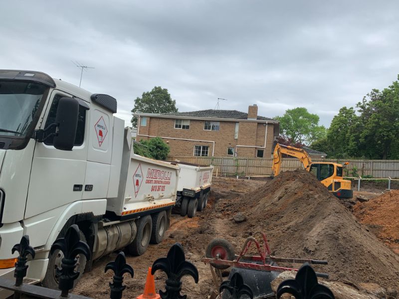 Residential site with excavation equipment, soil preparation, and materials delivery for concrete slab construction