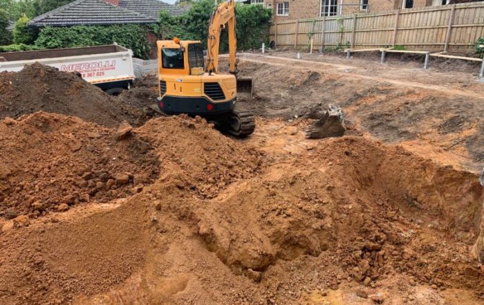 Yellow excavator performing soil management and ground preparation in residential setting